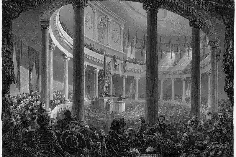 {'de': 'Volle Sitzreihen und Ränge in einem runden Saal mit Säulen und Fahnen, Das Innere der Paulskirche als Parlamentshaus, Stahlstich, 1848.'}