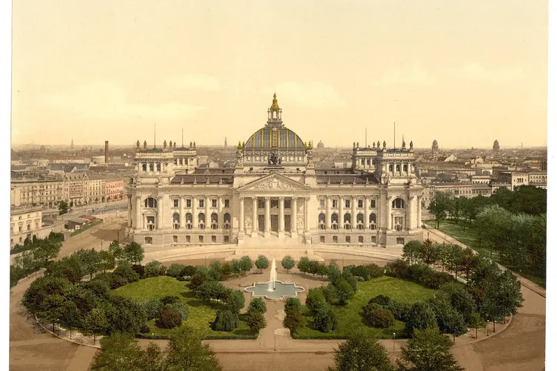 {'de': 'Großes Kuppelgebäude mit Säulenportikus, davor eine Parkanlage mit Springbrunnen und Bäumen, Reichstag House Berlin, Photochrom, 1890.'}